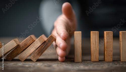Businessman Preventing Domino Effect By Inserting Hand Between Falling And Upright Wooden Blocks In Close-Up Visual Image.