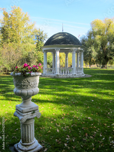 Park rotunda with red flowers in vase, sunny day.
