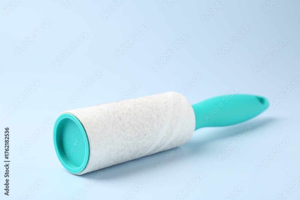 Fototapeta premium Lint roller with used sticky tape on light blue background, closeup