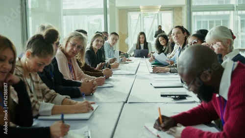 Business professionals attend a conference, actively engaged in discussions and note-taking. Individuals are focused, collaborating in a professional learning environment.