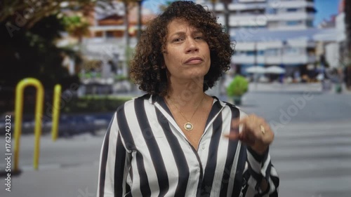 Woman pinches fingers to indicate a small size interval on a bustling urban street with crosswalk lines and modern building facades; uncertainty.