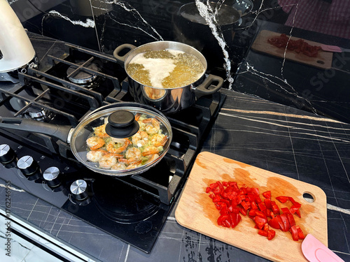 Photos Shrimps and pasta cooking on stove, tomatoes on countertop in kitchen