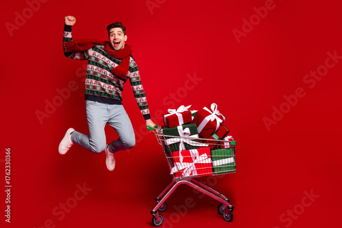 Quadro su tela Funny winter christmas man jumps with golden joy pushing a shopping cart full of