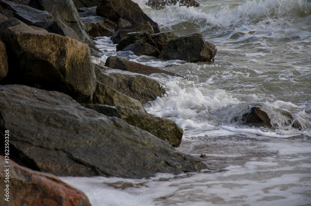 Fototapeta premium Rough ocean waves crashing against dark coastal rocks.