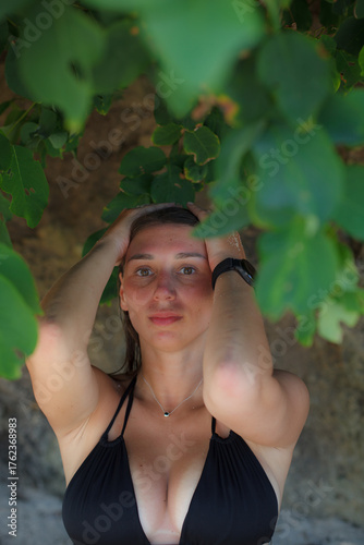 Close-up portrait of young woman in black bikini under green tropical leaves in Bali, Indonesia