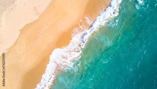 Aerial shot of a sandy beach meeting turquoise ocean waves. The sun reflects beautifully, illuminating the sand and the clear water