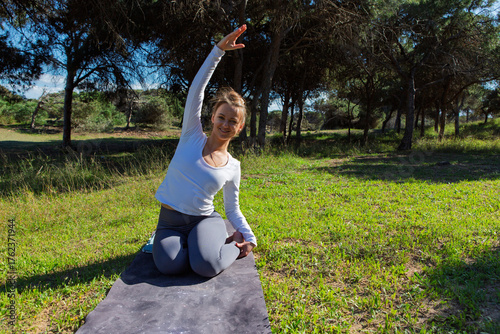 Smiling woman stretching sideways while kneeling on yoga mat outdoors