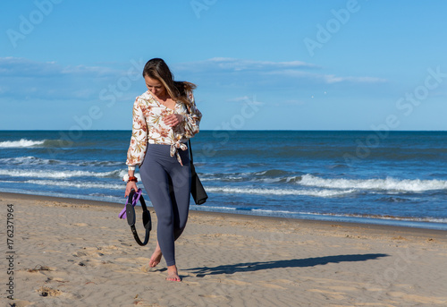 Woman walking barefoot on beach with fitness gear