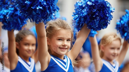 Smiling young girls in blue outfits hold bright blue pom-poms.