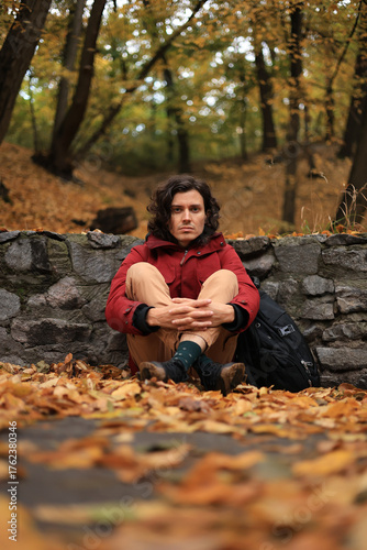 Young man sitting on the ground in autumn park