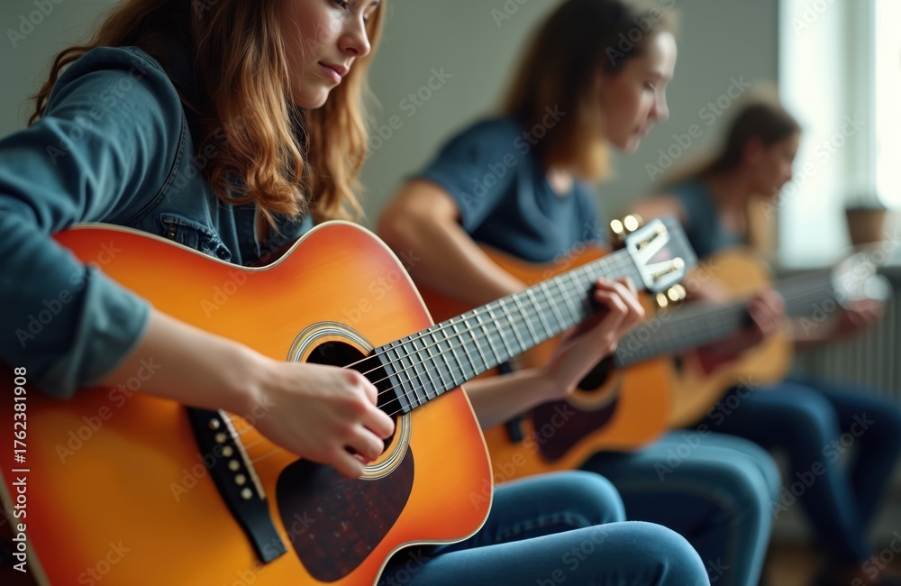 Fototapeta premium Three young women play acoustic guitars in a room. They focus on strumming chords and practicing together. Friends share musical hobby, enjoying group lesson.