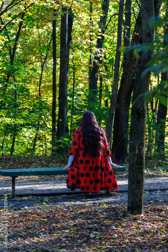 woman with long dark hair in ladybug coat sitting on the bench in autumn park