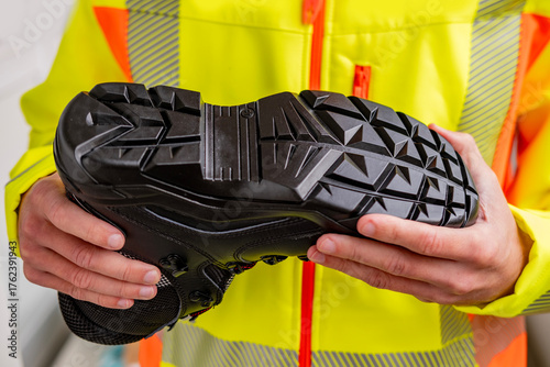 Canvastavla Worker in hi-vis vest holds black safety heavy-duty work boots with prominent re