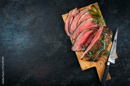 Traditional Commonwealth Sunday roast with sliced cold cuts roast beef with with cornichon pickle served as top view on a wooden board with copy space left