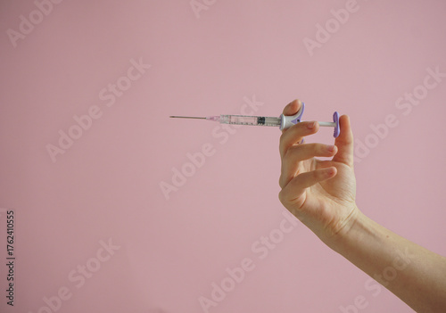 gloved hand holding multiple colorful syringes, against a soft background. Conceptual image related to medicine, beauty injections, or cosmetic procedures