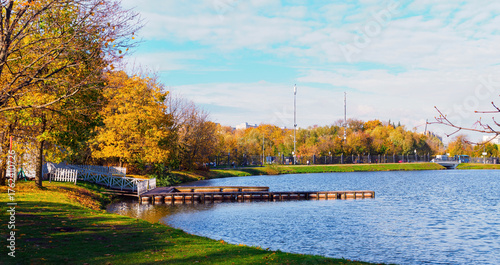 A boat dock on the shore of a pond in a city park in autumn - panorama.