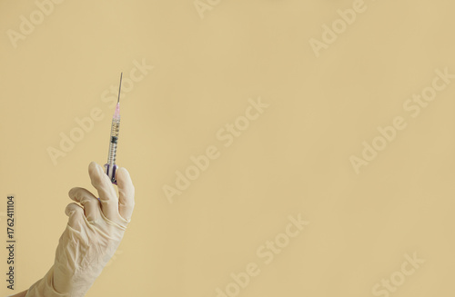 gloved hand holding multiple colorful syringes, against a soft background. Conceptual image related to medicine, beauty injections, or cosmetic procedures