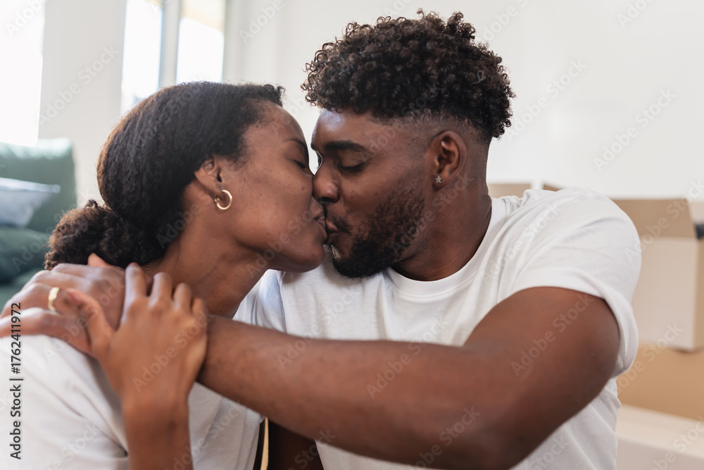 Fototapeta premium Loving couple sharing a tender kiss at home surrounded by moving boxes. Warm and intimate moment symbolizing love, connection, and the joy of starting a new life together