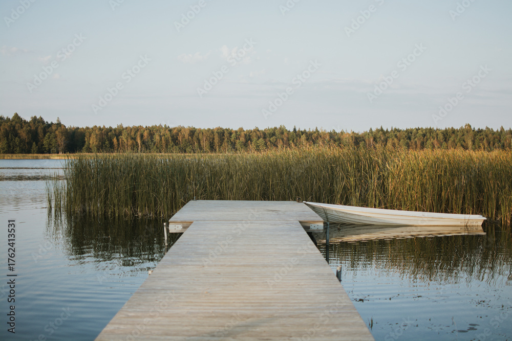 Naklejka premium Wooden pier and boat on a calm lake in summer in Estonia