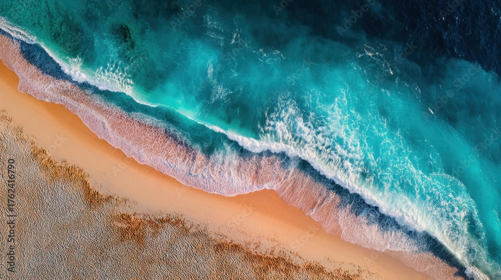 Fototapeta premium Aerial View of Ocean Waves Gently Crashing on Serene Sandy Beach with Vivid Blue Water and Soft White Foam at Coastal Paradise