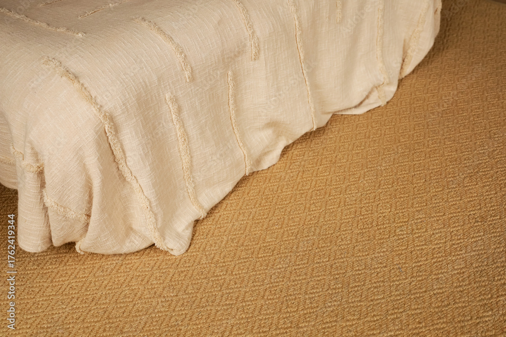 Obraz premium Soft beige bedspread drapes over a textured golden rug in a calm bedroom setting