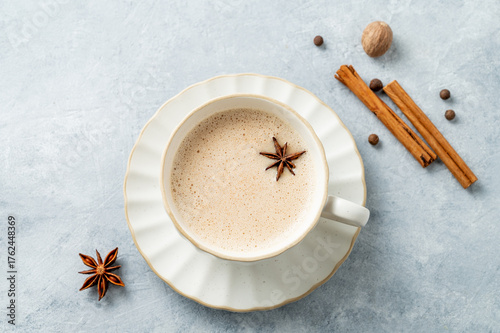 Fototapeta Naklejka Na Ścianę i Meble -  Traditional Indian masala chai tea with milk and spices in a white cup on a light background close up.