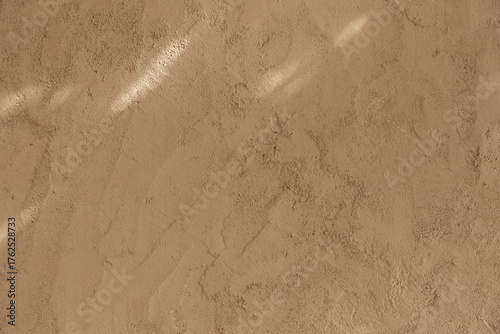Close-up of a beige plaster wall texture illuminated by soft natural light and subtle shadows. Minimal and warm surface background ideal for design, architecture, and texture references.