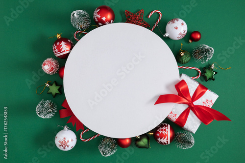 Festive Christmas composition with gifts, balls and fir branches on green background. White circle in the center for text. Ideal layout for greetings, banners and cards.