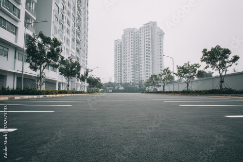 Minimal rooftop parking lot on a misty day, wet asphalt surface reflecting soft light, surrounded by tall modern buildings.