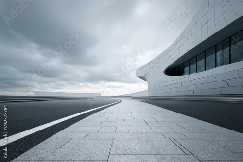 Minimalist three-story glass building standing at the end of a wet asphalt track, surrounded by misty hills under soft morning light.