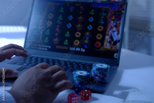 Close-up of a man's hands playing online slot gambling in front of a laptop with a stack of dice and poker chips, ready to express his victory. The concept of gambling. Winning and losing in gambling.