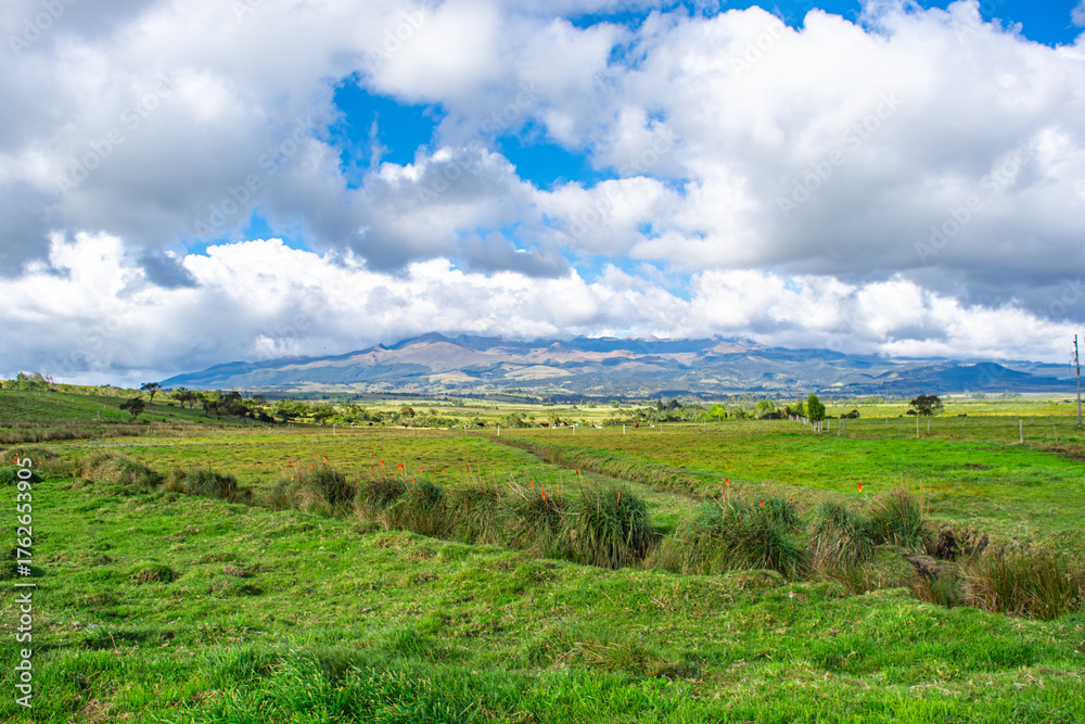 Fototapeta premium Scenic view of lush green fields with mountains under a stunning cloudy sky in Puracé, Cauca, Colombia.