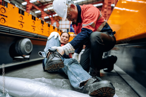 Injured employee receiving assistance from colleague in manufacturing facility after workplace injury. Industrial accident concept showing teamwork and safety awareness in workplace environment.