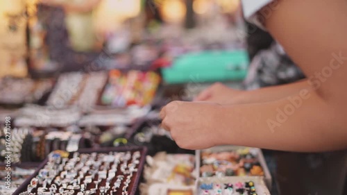 Young girl closeup hands choosing jewelry and souvenirs during travel through tourist city on open street market fair