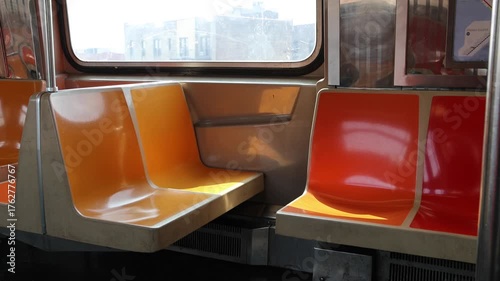 empty seats and looking out the window of moving elevated subway train in new york city nyc brooklyn metro commute pov move ride riding nobody yellow orange red seats d line passing buildings