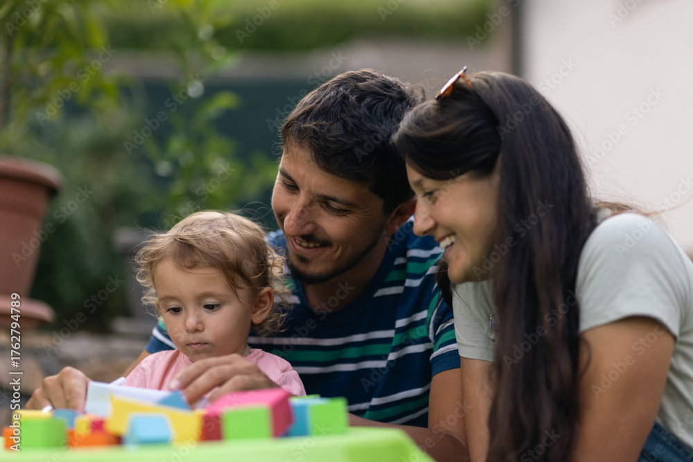 Obraz premium Smiling Family Bonding While Playing With Colorful Building Blocks Outdoors on a Bright Day