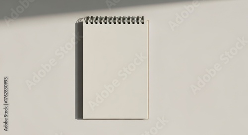 A blank notebook, wire-bound, in sunlight, on a neutral surface