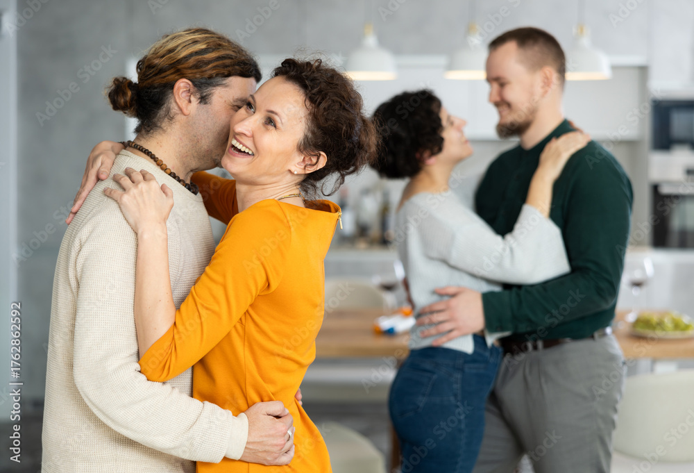 Fototapeta premium Two married couples dance during holiday, have fun, move and jump in dining room. Family event is held with fun music and dancing