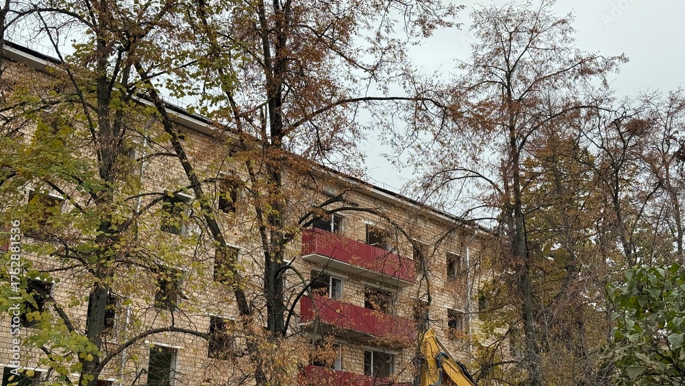 Obraz premium Old brick residential building with red balconies and autumn trees. Concept of urban decay, renovation and city transformation 