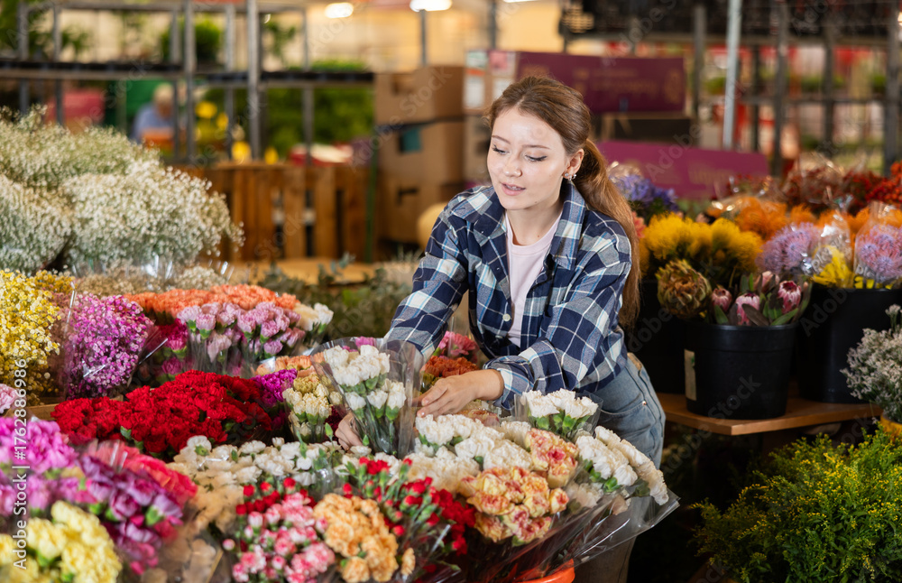 Obraz premium Girl salesman takes out bunch of carnation from showcase, creates bouquets, combines flowers and decorative herbs. Supply and demand, assortment of flowers for ceremonial and ritual bouquets.