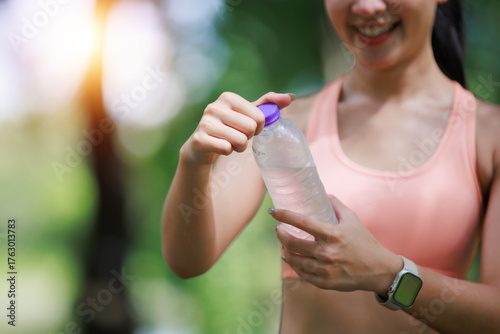 Fotografi Woman opening a water bottle, staying hydrated during an outdoor fitness workout