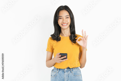 Smiling asian woman holding smartphone and shows ok sign on white background.