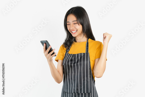 Happy Asian woman owner in black apron standing with holding smartphone on white background.
