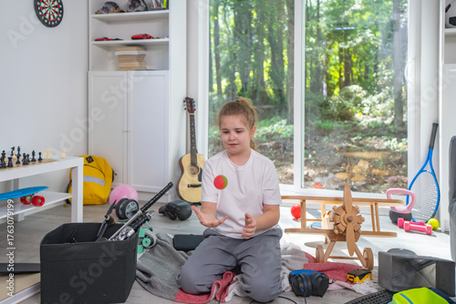 Child cleaning messy playroom at home. Kid organizing scattered toys on the floor. Kid helping tidy up children room. Boy cleaning untidy playroom interior. Funny child picking up toys in messy room.