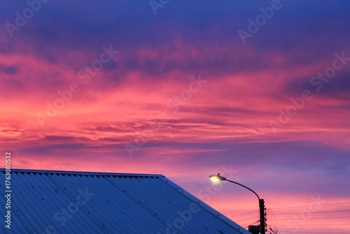 Atardecer dramático con cielo rojizo sobre un techo y un poste de luz.