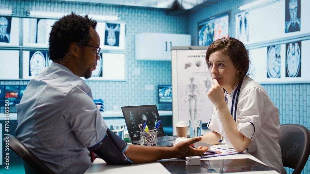 Obraz premium Woman specialist taking pulse and blood pressure for african american patient, consulting a man during check up visit. Doctor doing a cardiac control measurements, blood pressure monitor. Camera B.