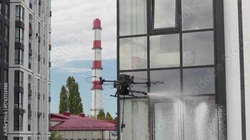 Industrial drone spraying water while cleaning glass facade of modern building exterior