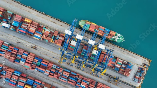 Aerial top view of shipping container terminal with cranes loading cargo ships in harbor