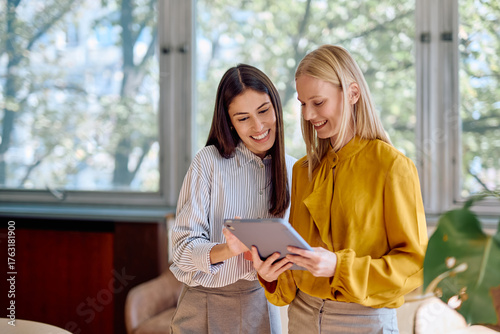 Canvas Print Two smiling businesswomen discussing work and sharing ideas while looking at a d