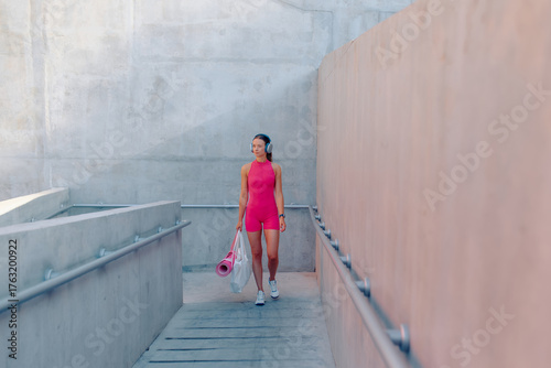 Woman walking down outdoor stairs in sports attire, carrying yoga mat and bag after workout session
